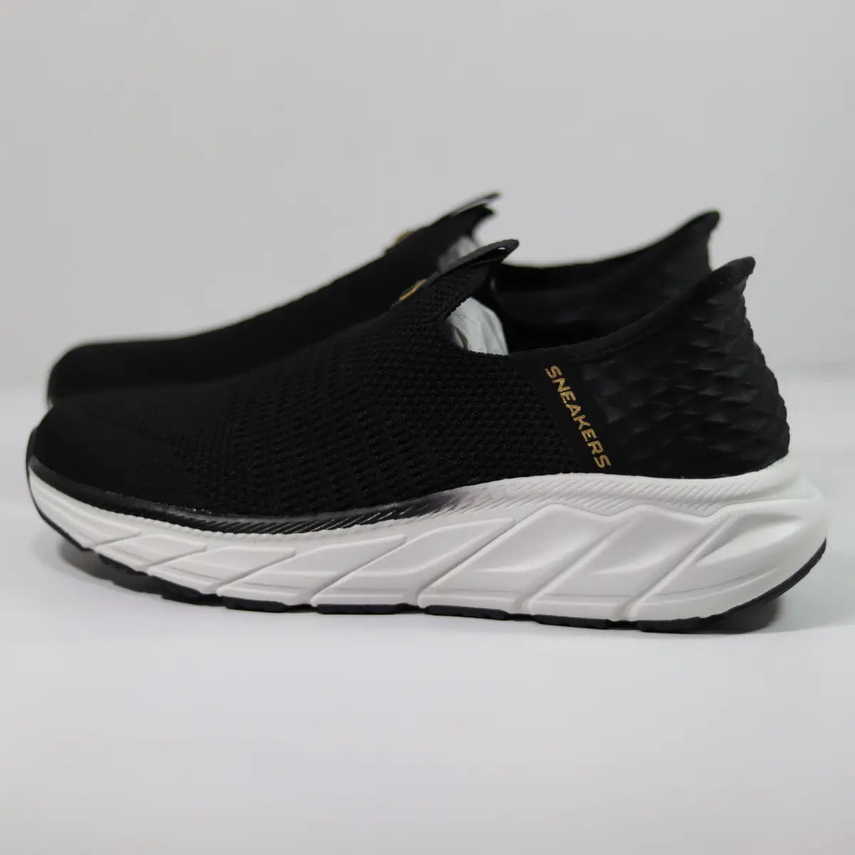 Par de zapatillas sin cordones mujer negras con suela gruesa blanca y texto dorado Sneakers Supply